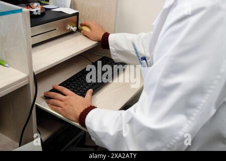 Médecin masculin en manteau blanc tapant sur ordinateur avec la main à proximité Banque D'Images