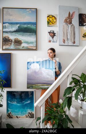 Femme pensive sérieuse avec toile fait une composition artistique créative à partir de peintures sur le mur de studio. Banque D'Images