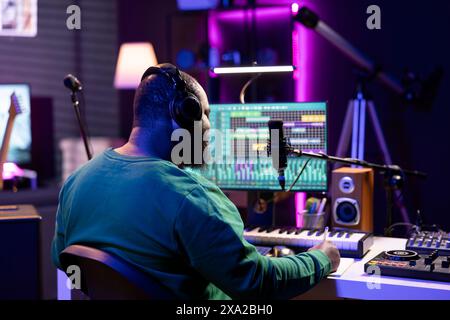 Jeune artiste producteur écrivant des paroles et des notes musicales pour créer de nouvelles pistes dans le home studio, en pensant à l'acoustique et aux lignes pour une bande originale moderne et cool. Compositeur composant des pistes avec un équipement. Banque D'Images