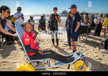 Un heureux handicapé asiatique parasurfer américain est transporté dans un fauteuil roulant spécial avec de grands pneus de plage à Huntington Beach, CA. Parasurfing ou ad Banque D'Images