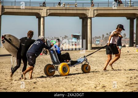 Un parasurfer est transporté dans un fauteuil roulant spécial avec de grands pneus de plage à Huntington Beach, CA. Le parasurf ou surf adaptatif est une forme de surfi Banque D'Images