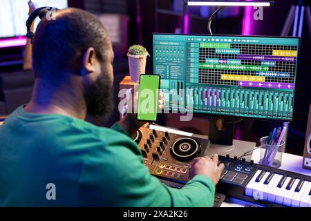 Technicien masculin utilisant une console de mixage et un piano pour éditer des airs, ayant un écran de maquette isolé. Compositeur produisant de la nouvelle musique avec des techniques de mixage et de mastering dans son home studio. Banque D'Images