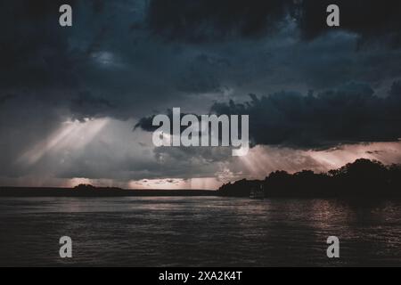 Une image époustouflante capturant l'interaction dramatique de la lumière et des nuages d'orage sur le fleuve Zambèze au coucher du soleil avec les rayons du soleil perçant à travers l'obscurité s. Banque D'Images