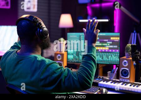 Technicien audio afro-américain qualifié compte à rebours avant d'enregistrer une chanson, faisant une session dans son home studio. Producteur fonctionnant sur console de mixage et logiciel numérique, équipement stéréo. Banque D'Images