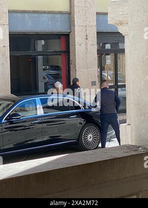 Cremona, Italie - 2 mai 2024 un chauffeur en costume et un garde de sécurité escortent un couple âgé d'une voiture de luxe noire devant une construction moderne Banque D'Images