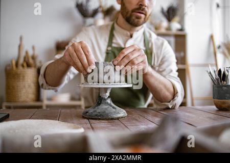 Gros plan des mains de l'artisan masculin portant un tablier travaille avec l'argile. Banque D'Images