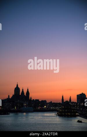 Coucher de soleil sur la rivière IJ avec la silhouette de la basilique Saint-Nicolas au loin - Amsterdam, pays-Bas Banque D'Images