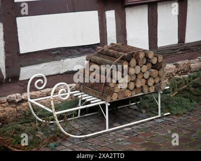 Un tas de bois sur un traîneau en métal blanc devant une vieille maison à colombages, kandel, allemagne Banque D'Images