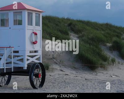 Une tour de sauvetage blanche avec un toit rouge se dresse sur une plage de sable en face de dunes vertes, Baltrum Allemagne Banque D'Images