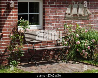 Un banc en bois à côté de rosiers devant un mur de briques rouges avec une fenêtre, Baltrum Allemagne Banque D'Images