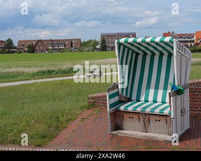 Une chaise de plage verte et blanche se dresse sur une place pavée avec des maisons en arrière-plan, Baltrum Allemagne Banque D'Images