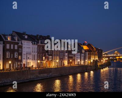 Maisons de ville le long d'une rivière la nuit, fenêtres éclairées reflétées dans l'eau, atmosphère calme, Maastricht, pays-Bas Banque D'Images