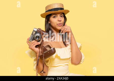 une femme robe inyellow et chapeau prenant des photos par appareil photo vintage sur un fond jaune. Des gens heureux qui partent en vacances, vacances Banque D'Images