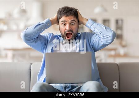 Homme choqué réagissant à l'écran de l'ordinateur portable tout en étant assis sur le canapé Banque D'Images