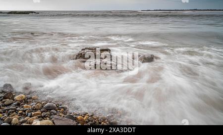 Vagues se brisant sur une plage de galets, avec de multiples galets colorés sur le rivage Banque D'Images