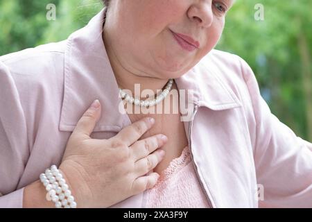 femme mature, 55 ans, élégamment habillée de rose se sentant malade, éprouvant des bouffées de chaleur et de l'inconfort de la ménopause, des problèmes de santé féminine, le vieillissement grac Banque D'Images