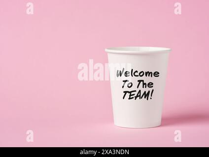 Bienvenue dans le message de l'équipe sur une tasse de café en papier sur fond rose. Message d'accueil par le nouveau lieu de travail ou les coéquipiers. Banque D'Images