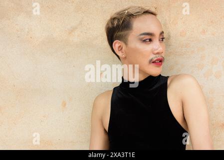 Portrait d'un bel homme asiatique de soutien de la communauté LGBT queer avec moustache portant rouge à lèvres et combinaison sur fond de mur beige Banque D'Images