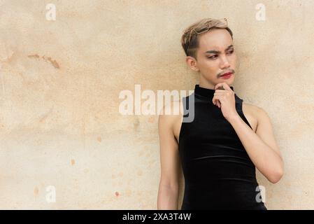 Portrait d'un bel homme asiatique de soutien de la communauté LGBT queer avec moustache portant rouge à lèvres et combinaison pensant sur fond de mur beige Banque D'Images