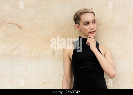 Portrait d'un bel homme asiatique de soutien de la communauté LGBT queer avec moustache portant rouge à lèvres et combinaison sur fond de mur beige Banque D'Images