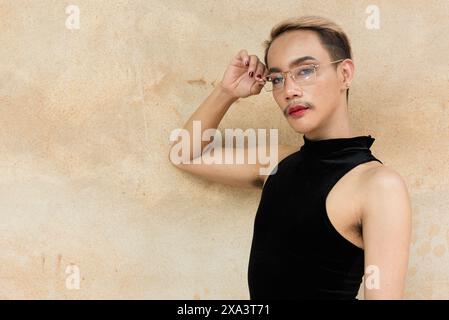 Portrait d'un bel homme asiatique de soutien de la communauté LGBT queer avec moustache portant rouge à lèvres et combinaison sur fond de mur beige Banque D'Images