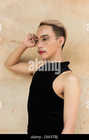 Portrait d'un bel homme asiatique de soutien de la communauté LGBT queer avec moustache portant rouge à lèvres et combinaison sur fond de mur beige Banque D'Images