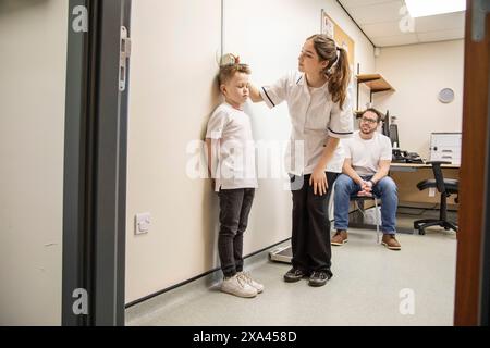 L'enfant est mesuré lors d'un bilan médical comme le père observe. Banque D'Images