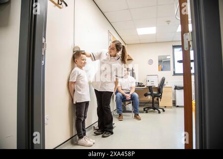 L'enfant est mesuré lors d'un bilan médical comme le père observe. Banque D'Images