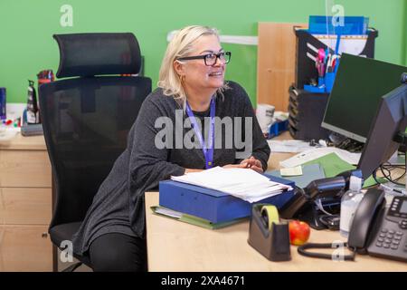 Femme souriante au travail avec ordinateur et papiers dans le bureau d'un cabinet médical Banque D'Images