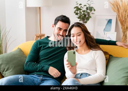Couple regardant un smartphone sur un canapé. Banque D'Images