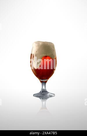 Gobelet en verre débordant d'artisanat, bière brune, surmonté d'une mousse épaisse et crémeuse sur fond blanc de studio. Banque D'Images