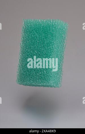 Éponge de nettoyage texturée de couleur turquoise flottant en milieu d'air sur fond gris Banque D'Images