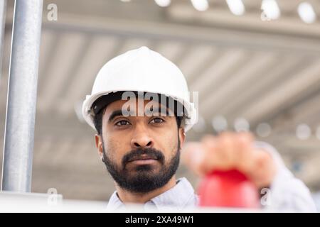 Un homme concentré portant un casque blanc regarde attentivement quelque chose, en appuyant sur le bouton rouge Banque D'Images