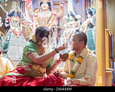 Au cours d'un service de Valaikappu, une femme enceinte nourrit son mari à partir d'une noix de coco fendue. Dans un temple hindou à ozone Park, Queens, New York. Banque D'Images