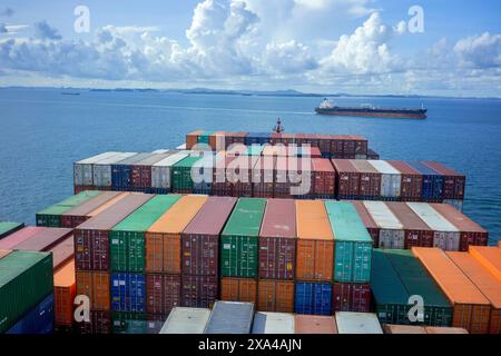 Un cargo empilé haut avec des conteneurs d'expédition colorés navigue à travers l'océan sous un ciel bleu nuageux. Banque D'Images