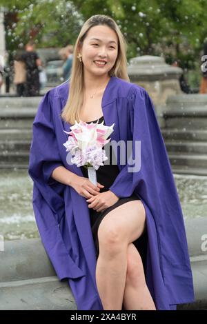 Après la cérémonie de remise des diplômes de NYU 2024, une belle femme asiatique américaine pose pour des photos tout en tenant des fleurs. Dans Washington Square Park à Manhattan Banque D'Images