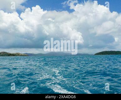 Paysage marin vibrant avec des eaux bleues claires sous un ciel nuageux dynamique, avec des îles vertes lointaines à l'horizon. Banque D'Images