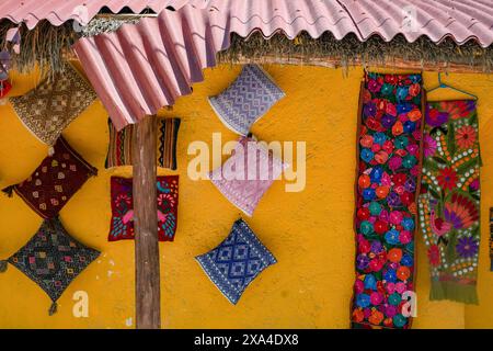 Une variété de textiles colorés sont exposés sur un mur orange vibrant sous un toit ondulé avec des textiles suspendus. Banque D'Images