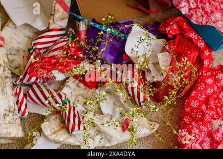 Un arrangement encombré de papier d'emballage de cadeau de Noël coloré, de rubans et de noeuds dispersés sur le sol, indiquant une session récente de déballage. Banque D'Images