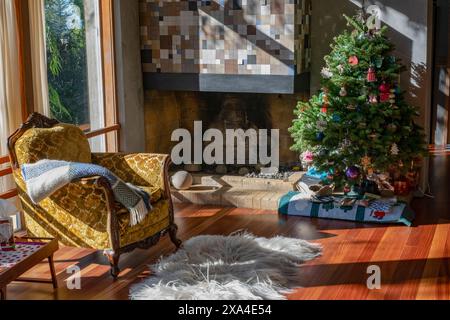 Un salon confortable décoré pour Noël avec un arbre de fête, une cheminée et un fauteuil drapé d'une couverture. Banque D'Images