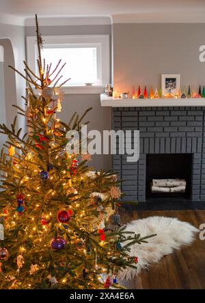 Un sapin de Noël bien décoré se dresse dans une pièce confortable avec une cheminée allumée et une série de bougies allumées sur la cheminée. Banque D'Images