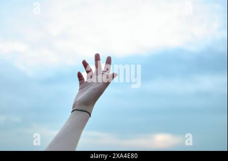 Une main tendue atteint un ciel bleu avec des nuages tortueux. Banque D'Images