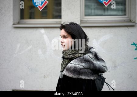 Une femme marche devant un bâtiment avec des graffitis sur le mur, expirant son souffle visible dans l'air froid. Banque D'Images