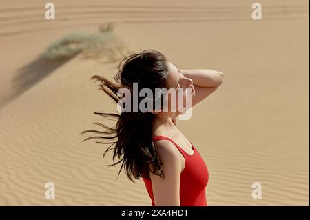 Une femme se tient dans un désert, ses cheveux soufflant dans le vent, alors qu'elle regarde au loin avec une expression réfléchie. Banque D'Images