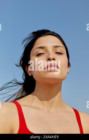 Une femme avec ses cheveux soufflant doucement dans la brise est debout contre un ciel clair, regardant au loin avec une expression sereine. Banque D'Images