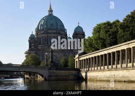 L'image montre la cathédrale de Berlin (Berliner Dom) avec son grand dôme et ses tours jumelles, vue de l'autre côté de la rivière Spree, avec un pont de pierre à gauche et une colonnade classique longeant la rive. Banque D'Images