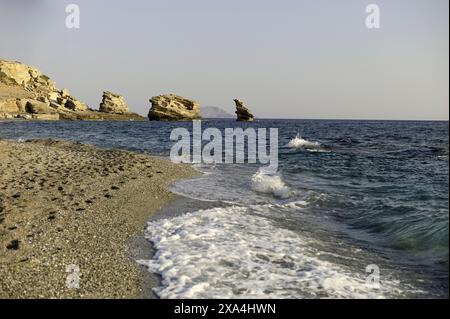 Plage sereine avec des vagues douces lavant sur la rive sablonneuse, avec des falaises accidentées en arrière-plan sous un ciel clair. Banque D'Images