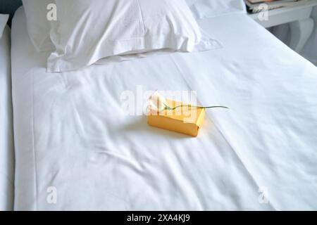 Un lit soigneusement fait avec des draps blancs avec un seul cadeau emballé avec ruban jaune en son centre. Banque D'Images