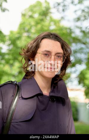 Une jeune femme souriante avec des cheveux bruns à la longueur des épaules portant des lunettes et un haut violet, avec des arbres en arrière-plan. Banque D'Images