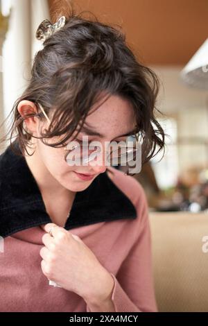 Une jeune femme avec des lunettes regarde bien vers le bas, ses cheveux attachés de façon décontractée, portant un haut de couleur rose avec un col foncé. Banque D'Images